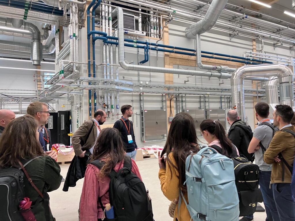 Site visit of the Swedish BioReCer stakeholders at RISE. They are inside a huge hall with silver tubes on the walls and the ceiling.
