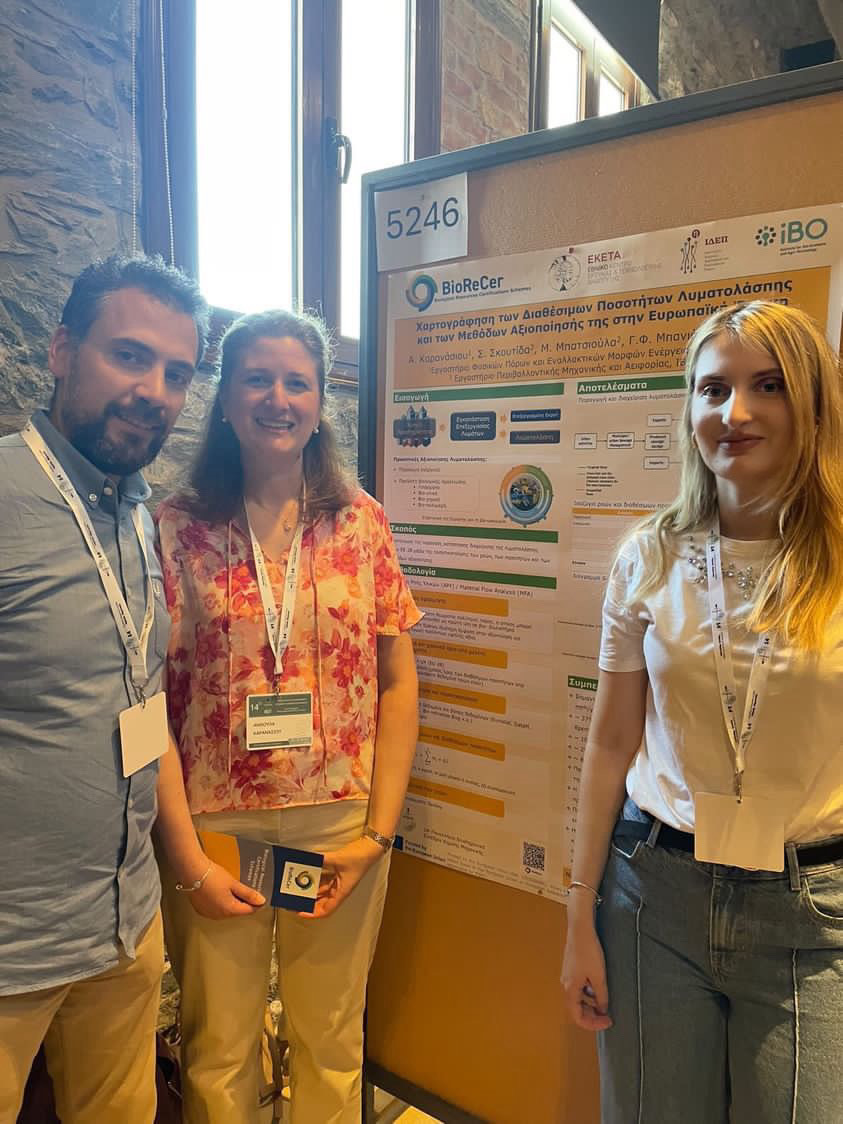 Sotiris Patsios, Anthoula Karanisou and Stamatia Skoutida from CERTH in front of their BioReCer poster at the Panhellenic Conference on Chemical Engineering in Thessaloniki 2024. Sotiris with dark hair and a beard and Anthoula with dark-blonde hair are on the left side of the poster. They are about 40 and wear colourful business outfits in blue and orange. Stamtia, a young woman with blonde hair is on the right side of the poster and wears a white shirt and a blue jeans.