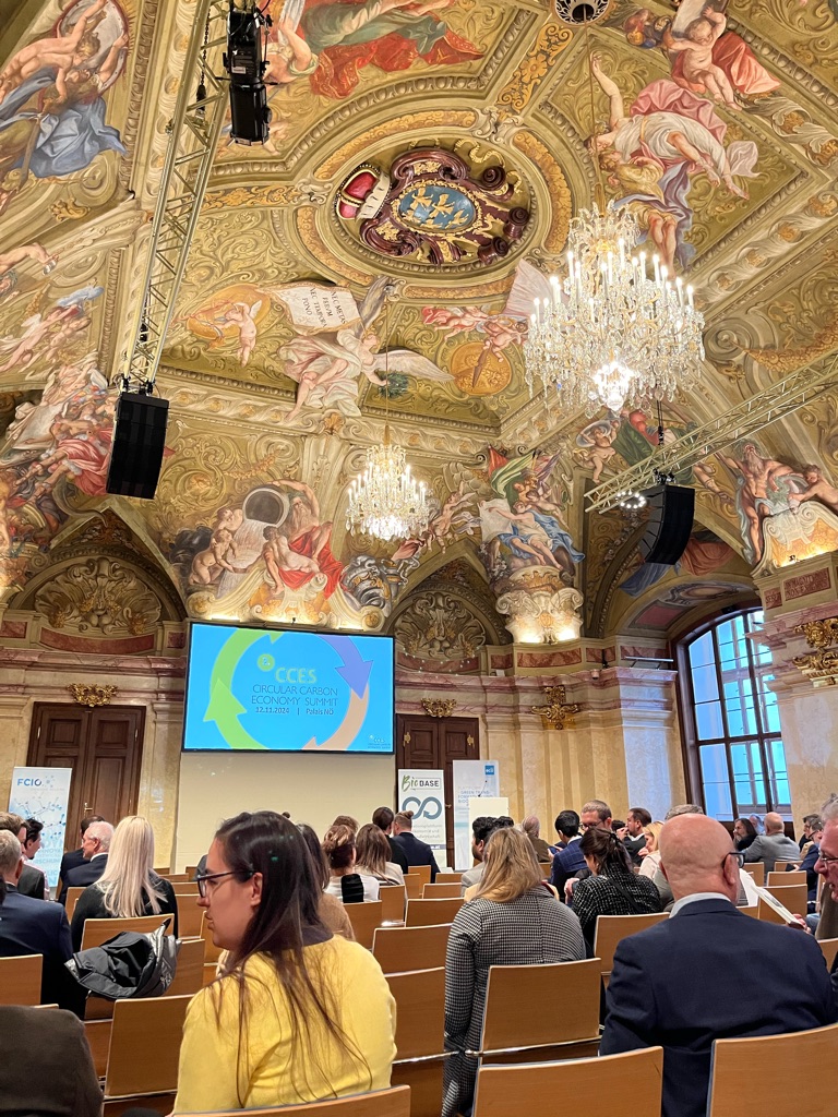 Participants at the Circular carbon Economy Summit in Vienna 2024. View from the back of the baroque venue room (Palais Niederösterreich). Participants are sitting on chairs facing a screen and the panel.